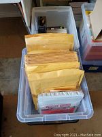 Clear plastic bin with multiple yellow bubble mailers of various sizes along with some plastic wrapped notebooks or pads.