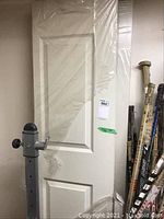 Photo showing one of the two white hollow core bi-fold doors wrapped in plastic, with a visible raised panel design.