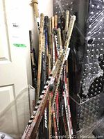 Full view of the large collection of curved hockey sticks leaning against a wall, showing varied brands and conditions.
