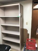 Full view of the beige metal shelving unit against a wall with various items around it.