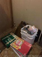 Assorted items on floor including reams of colored and lined paper and a white plastic bucket with coin rolling tubes and other office supplies.