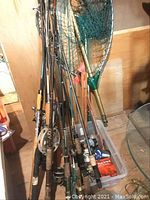 Cluster of rods leaning in corner with attached reels and plastic storage bin at base