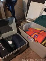 Metal storage box with three sleeping bags inside and a large plastic bin with life jackets