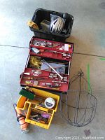 Overview of toolbox, metal hanging basket, yellow organizers with assorted tools, power cutout tool, and bike helmet in black plastic bin