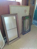 Full view of mirror leaning against wall with stained glass window and cork board behind