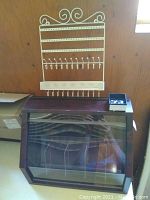 Wood and plexiglass jewelry display case with angled front window and white metal wall hanger placed on top.