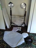 Two tripod light stands with dome reflectors placed side by side, wood rustic backdrop behind them, light bulbs and softboxes on floor in front