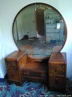 Front view of wood dresser with two side compartments each having drawer and cabinet door, central shelf, and large circular mirror attached at the back.