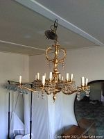 Wide view showing entire gold chandelier with decorative arms and some missing crystals