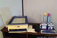 Yudu screen printing machine with accessories including inks, emulsion sheets, instructions, and packaging, arranged on a wooden surface.