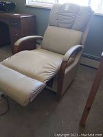 Full view of the beige leather recliner chair in a leaned-back reclining position with extended footrest, showing puffy backrest and wooden upholstered arms.