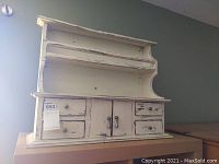 Front view of small wooden curio cabinet with white distressed paint and four drawers plus two doors