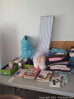 Overview photo showing table with stacks of fabric, a fabric cutting board, how-to books, and a turquoise pill shaver in plastic bag.