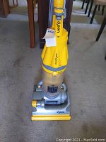 Front view of Dyson Root Cyclone upright vacuum cleaner showing yellow and gray body, clear dust bin, and upright handle.