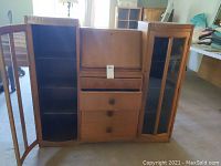 Front view of wooden secretary desk with both side glass door cabinets open showing shelving and three lower drawers with decorative scrollwork on one drawer.