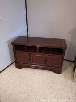 Front view of wooden television stand showing two open shelves and three cabinet doors with metal handles, scratches visible on top surface
