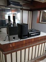 Full view of sound system components on countertop showing Sony receiver, Sony subwoofer, Altec Lansing powered subwoofer, and Altec Lansing speakers.