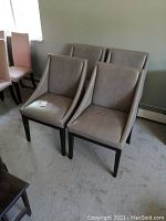 Four taupe/grey leather chairs from West Elm with curved backs and dark wooden legs arranged on carpet.