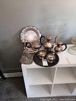 Full set of vintage silver plated tea and coffee service displayed on white shelf with two ornate serving trays and wine goblet, showing tarnishing and wear.