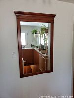 Front view of large wood framed mirror mounted on wall, shows reflective glass and wood frame detail