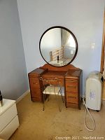 Full view of wooden vanity table with attached round mirror and metal frame chair with fabric seat in room corner showing wear and usage.