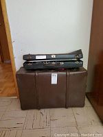 Brown hard-shell suitcase/trunk with black trumpet case stacked on top