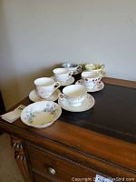 Six different floral china cups and saucers on a wooden surface