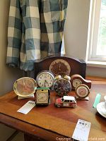 Photo showing the full group of 8 clocks on a table including a wooden mantel clock, metal alarm clocks, travel clocks, and a toy car clock