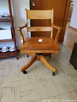 Front view of the solid wood swivel office chair showing backrest, armrests, and caster wheels under seat.