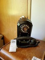 Front view of black antique rotary dial corded telephone showing handset placed on cradle on wooden surface.