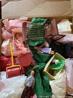 Box containing various miniature wooden dollhouse furniture pieces, small dolls, and a dustpan toy.