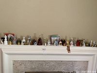 Front view of a variety of decorative bells lined up on a shelf, shows many small collectible bells including brass, glass, and ceramic.