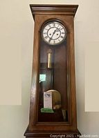 Full front view of oak-veneer case, dial and pendulum visible