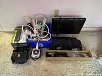 View of the entire lot showing multiple keyboards, power bars, an HP monitor, tripod in a box, black HP mouse, Sony clock radio, and binocular case.
