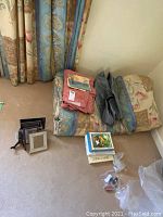 Full lot showing folded linens, assorted picture frames, boxes, and packaging material on a floral patterned cushion next to ornate curtains.