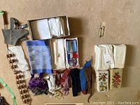 Wide view of scarves, ties, whistle pouch, assorted folded linens/fabrics, and small floral embroidered pieces