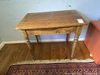 Front view of wooden table showing tabletop and one leg with scratches and wear.