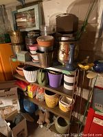 Shelf with various plant pots in ceramic, plastic and brass finish. Includes decorative items and boxed garden tools.