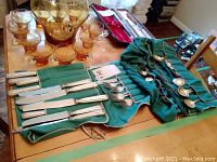 Overview of flatware on table showing knives, forks, spoons arranged on green storage mats with amber glass punch set in background