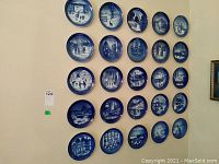 Wall display of 25 blue and white Royal Copenhagen collector plates arranged in a grid, showing various winter and holiday themed scenes.