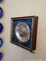 Side view of framed metal plate showing wood frame and glass front with etched building image.