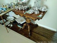 Full view of vintage wooden occasional table from front, showing carved pedestal base and items on top.