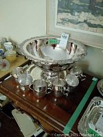 Photo showing the large punch bowl with six matching cups arranged around it on a wooden surface.