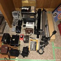 Wide shot of the entire camera equipment lot including cameras, tripods, cases, and lighting equipment.