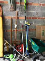 Photo showing variety of garden tools including pitchfork, shovel, Garden Claw tools, green chainsaw, leaf blower, and Yardworks spreader handle.