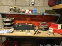 View of workbench surface showing Custom Craft jig saw, boxed power sander and circular saw attachments, toolboxes, hand tools, hardware, and small metal parts on pegboard and shelf.