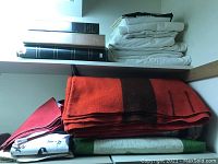 White linens and three photo albums on top shelf, blankets folded below.