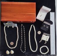 Full overview of cedar wood box with assorted pearl and sterling silver jewelry items arranged on black fabric including ruler and coin for scale.