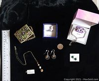 The entire lot shown together with ruler for scale; includes small ornate metal box, necklace, bracelets, earrings, and ring laid out on black fabric.
