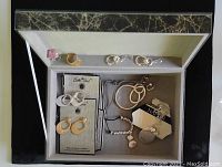 Box with gold vein pattern open showing assortment of sterling silver ring and costume jewelry including Bella Uno earrings, rings, necklaces and Napier pieces